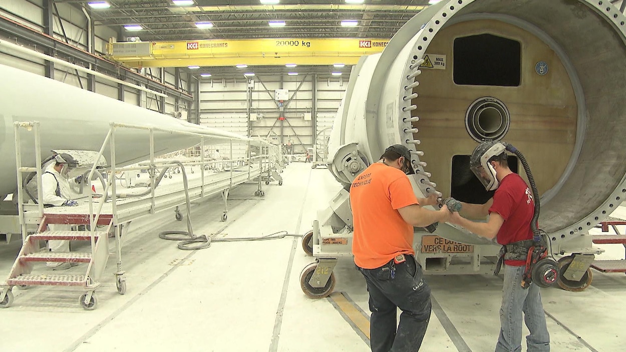 Deux employés travaillent près d'un élément de tour d'éolienne dans l'usine.