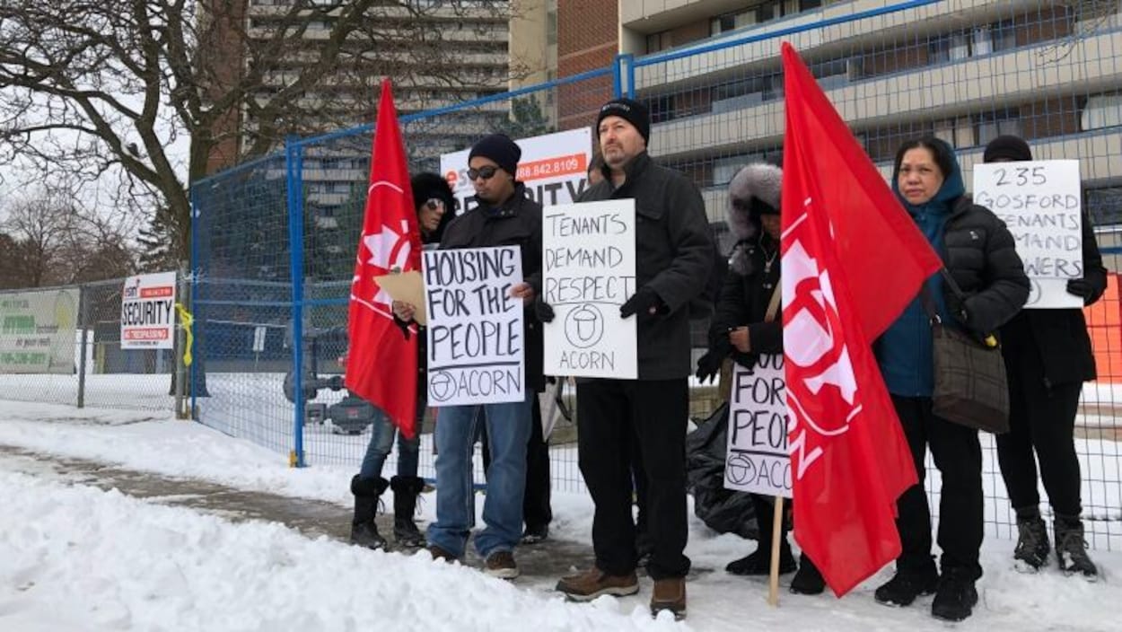 Une dizaine de personnes manifestent devant un immeuble avec des pancartes sur la neige.