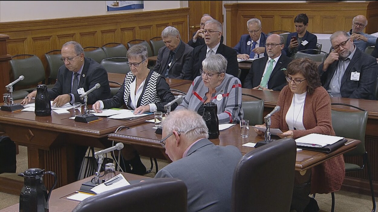 Quatre personnes assises à une table avec d'autres personnes derrière.