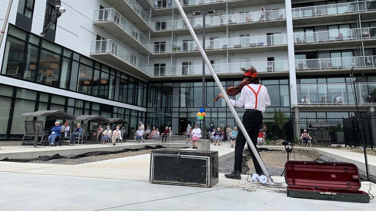 Un clown humanitaire joue du violon devant une résidence pour personnes âgées.