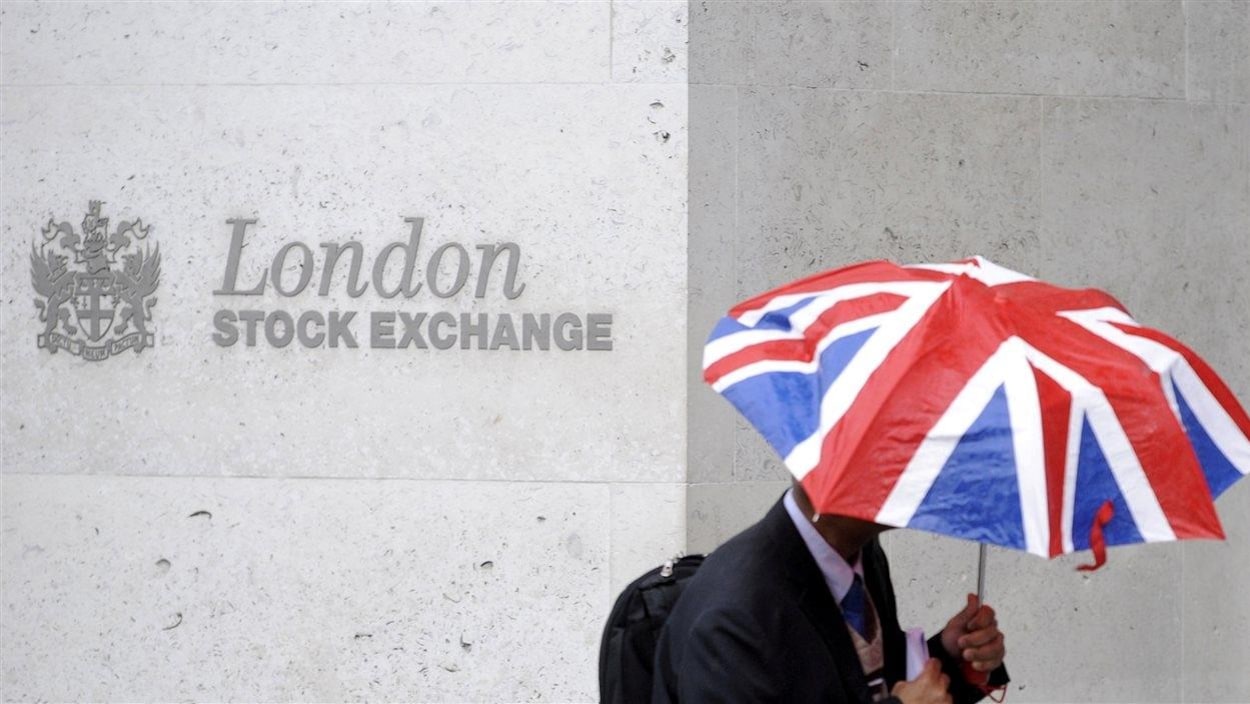 La façade de la bourse de Londres avec, devant, un passant s'abritant sous un parapluie aux couleurs du drapeau britannique.