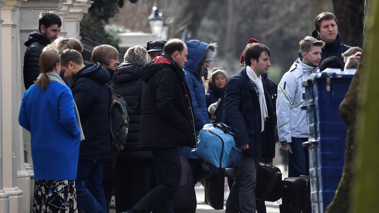 Devant l'ambassade russe à Londres, des jeunes gens habillés pour l'hiver assistent au départ des diplomates. Devant l'ambassade russe à Londres, des jeunes gens habillés pour l'hiver assistent au départ des diplomates.