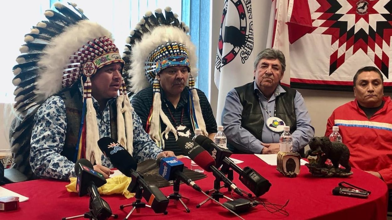 Deux hommes portant des coiffes de plumes devant de nombreux micros de journalistes.