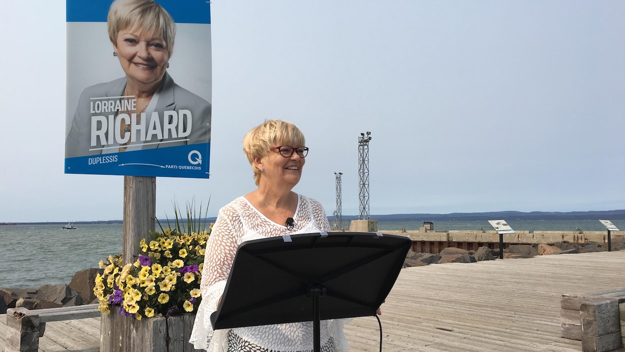 La députée sortante et candidate du Parti québécois dans Duplessis, Lorraine Richard, s'adresse aux médias avec en arrière-plan le Vieux-Quai de Sept-Îles et un bateau au large.