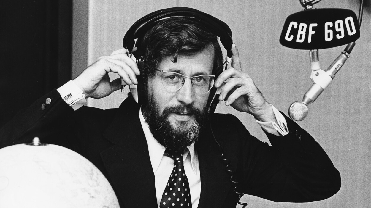 Dans un studio de radio, l'animateur Louis Martin ajuste un casque d'écoute sur sa tête. Un micro, portant une affichette avec la mention «CBF 690», est suspendu devant lui. Dans un studio de radio, l'animateur Louis Martin ajuste un casque d'écoute sur sa tête. Un micro, portant une affichette avec la mention «CBF 690», est suspendu devant lui.