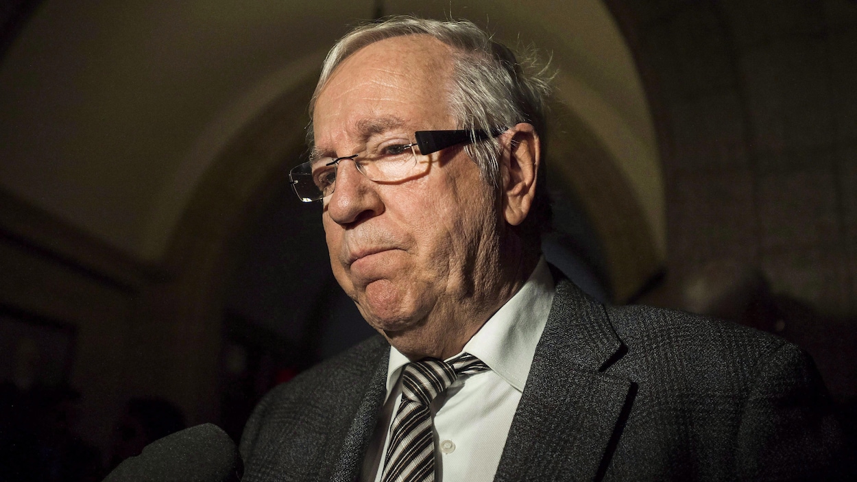 Un homme portant un complet et une cravate est interrogé par un journaliste dans un corridor du Parlement à Ottawa.
