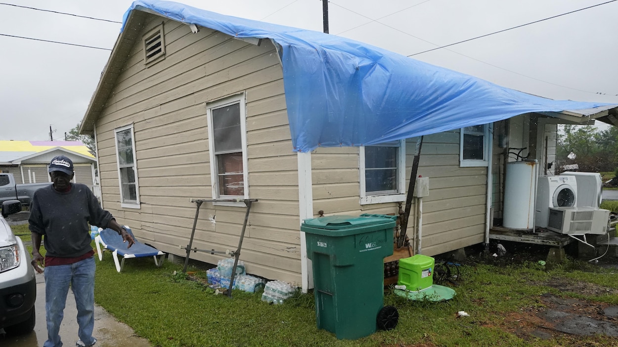 L'homme se tient à côté de sa maison, couverte d'une bâche.