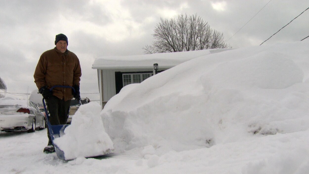 Luc Cayer pousse la neige de son entrée vers l'intérieur de son terrain avec une grosse pelle bleue.