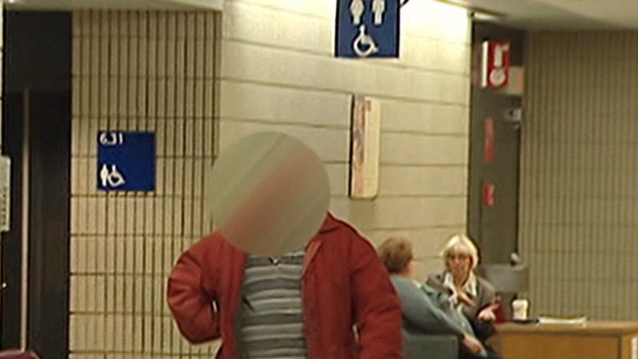Un homme au visage brouillé marche dans un couloir d'un palais de justice.