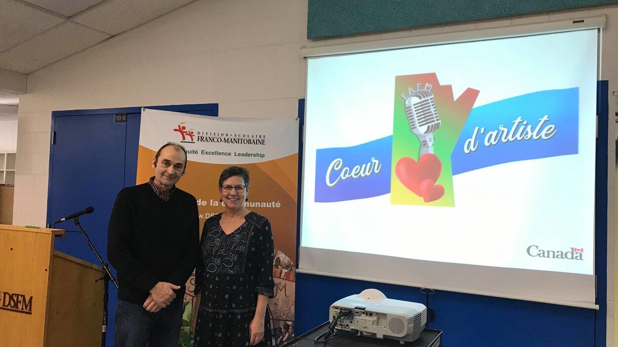 Un homme et une femme posent devant un écran qui projette le logo du concours « Coeur d'artiste ».