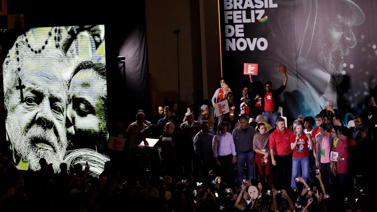 Une foule rassemblée dans un congrès, sur scène, des personnes sont massées devant le portrait de Luiz Inacio « Lula » da Silva.