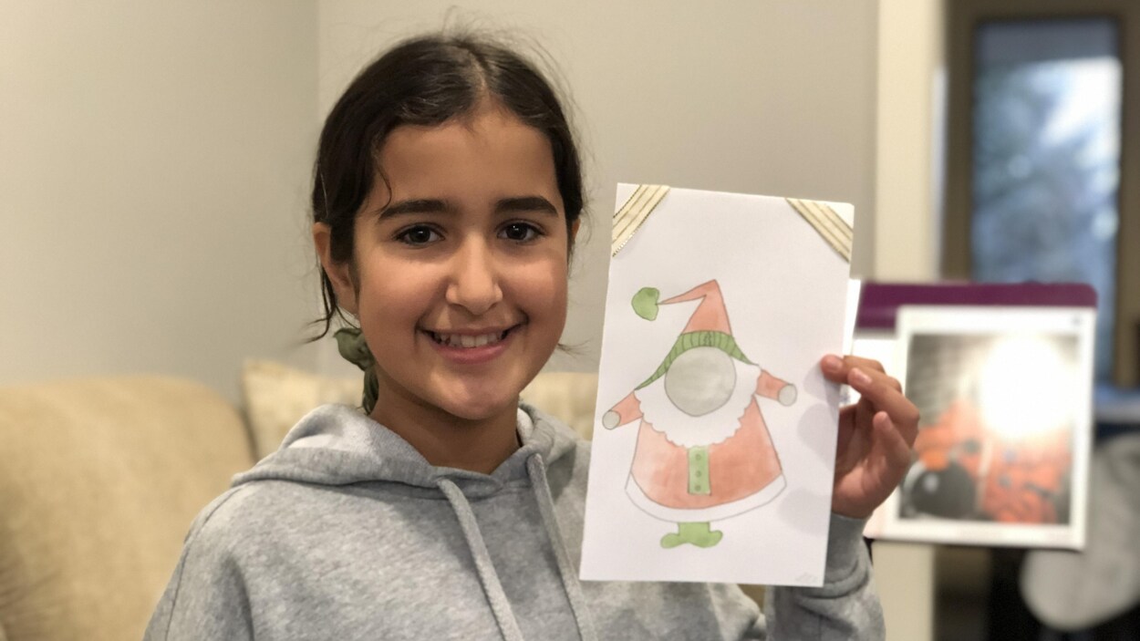 Lylia tient une de ses cartes dans sa main, sur laquelle elle a dessiné un gnome qui ressemble au père noël.