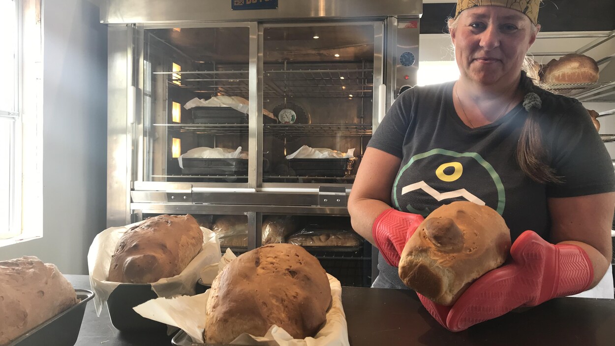 Lyne Bergeron tient une miche de pain et devant elle sur le comptoir reposent trois autres miches encore dans leur moule.