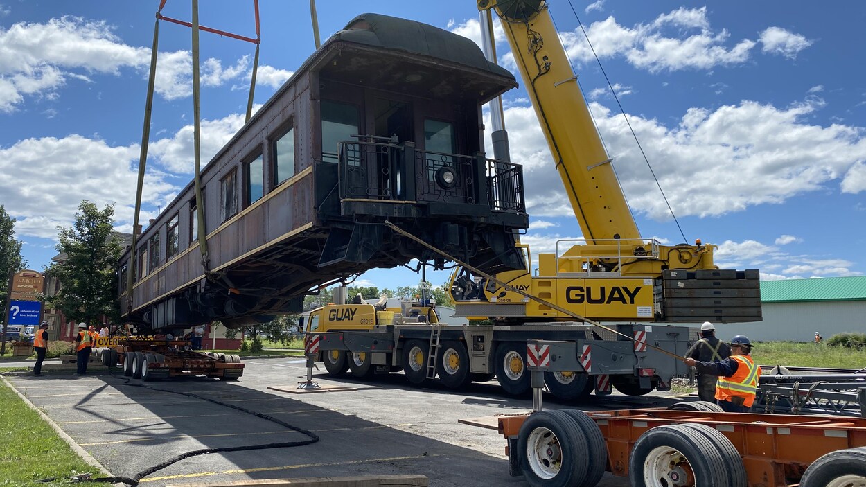 Un wagon de train est soulevé par une grue pour être installé sur un camion.