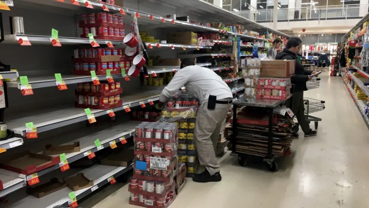 Un homme place des boîtes de conserve sur des tablettes vides.