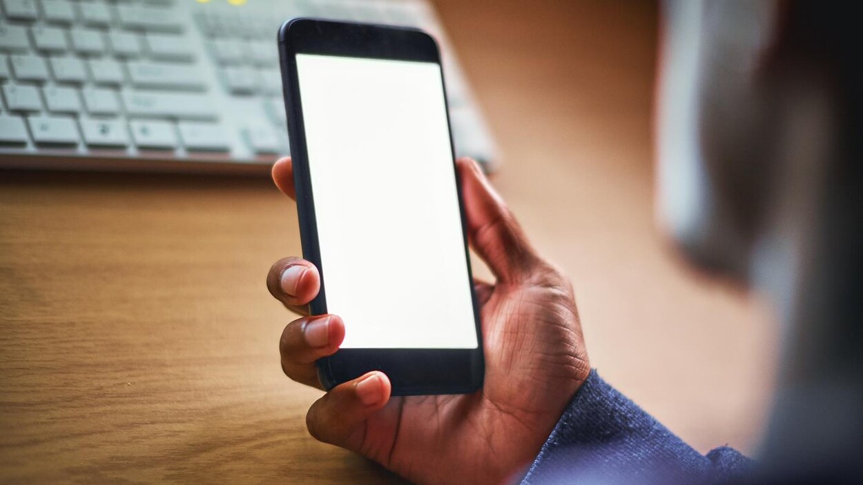 Un homme de profil regarde son cellulaire dans la pénombre.