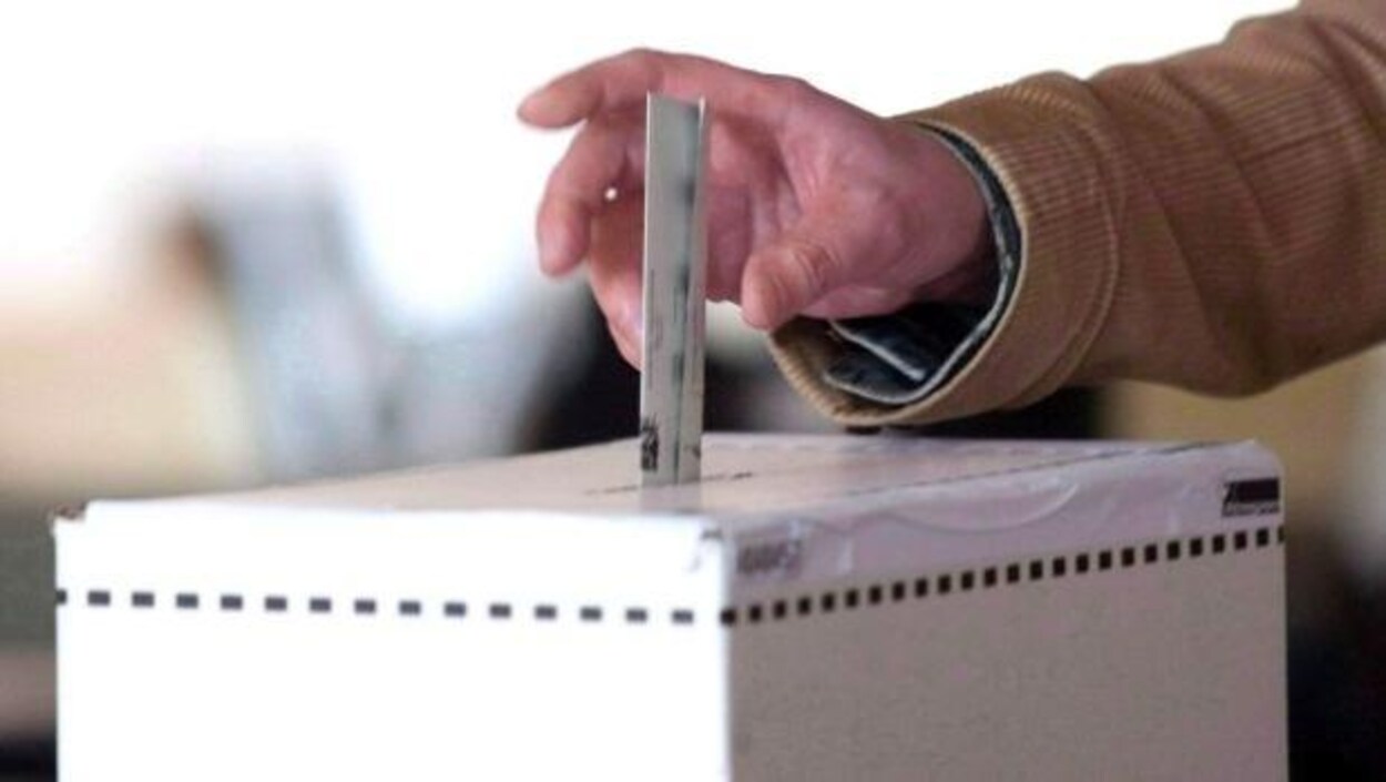 Une main dépose un bulletin de vote dans une boîte.