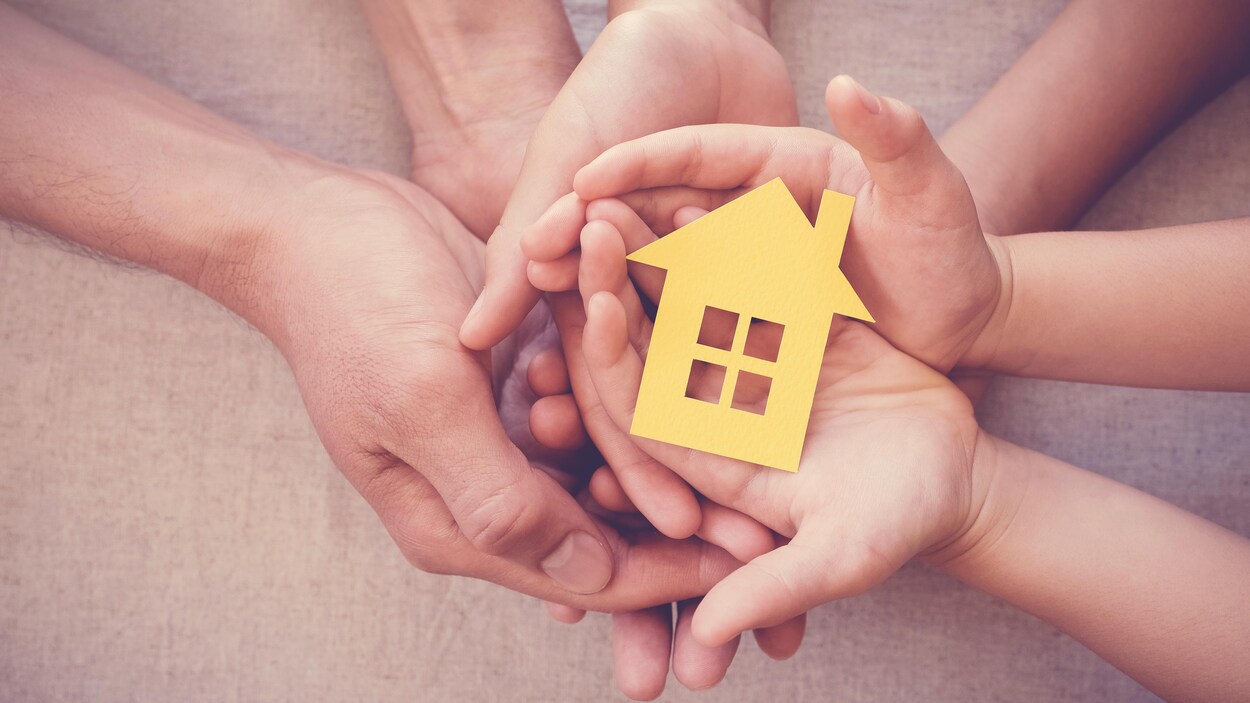 Des mains d'adultes et d'enfants tiennent dans leurs paumes une petite maison en carton.