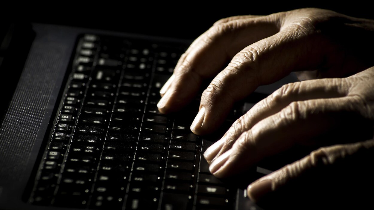 Les mains d'un vieil homme sur un clavier d'ordinateur portable.