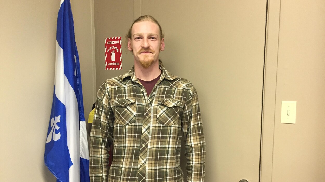 Un homme prend la pose à côté d'un drapeau du Québec.