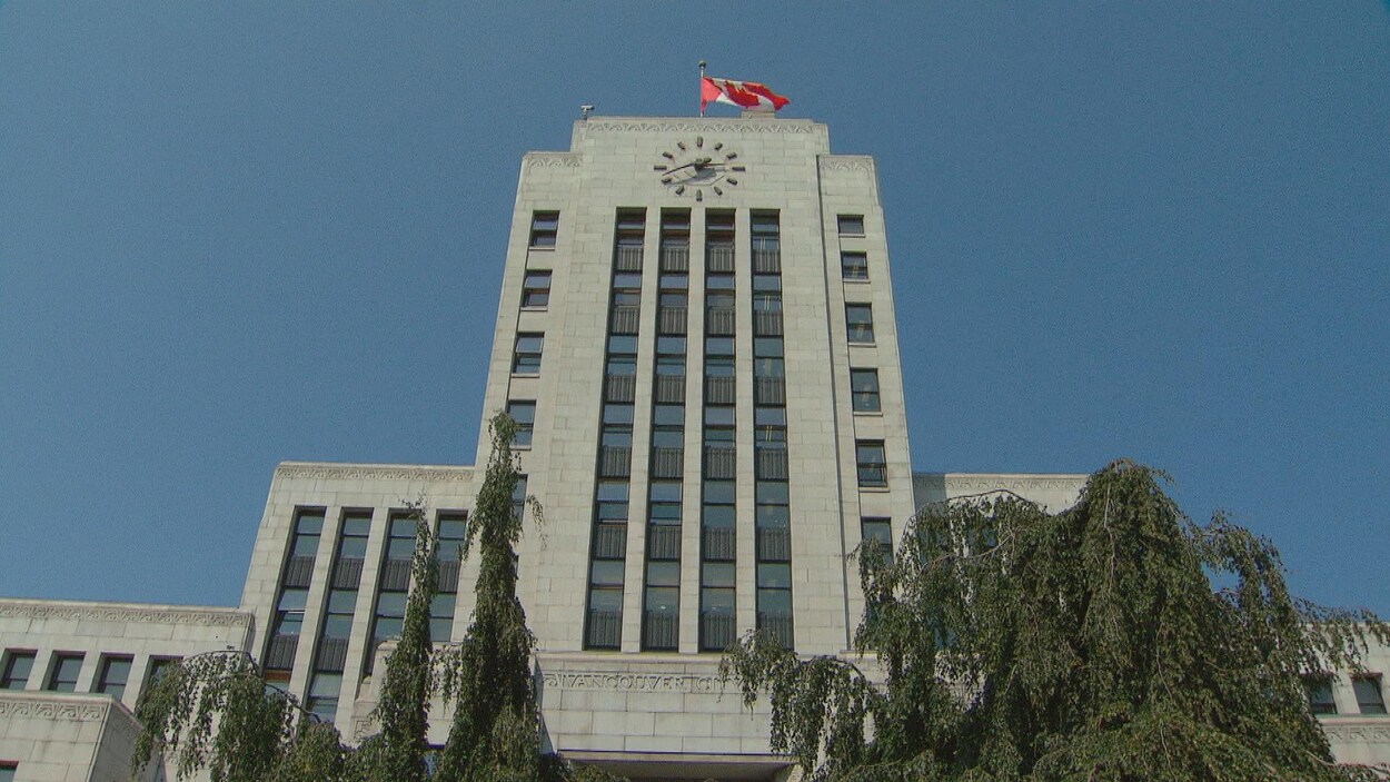 Plan en contre-plongée de l'hôtel de ville de Vancouver, un édifice en brique grise avec une imposante horloge et un drapeau canadien sur le toit.