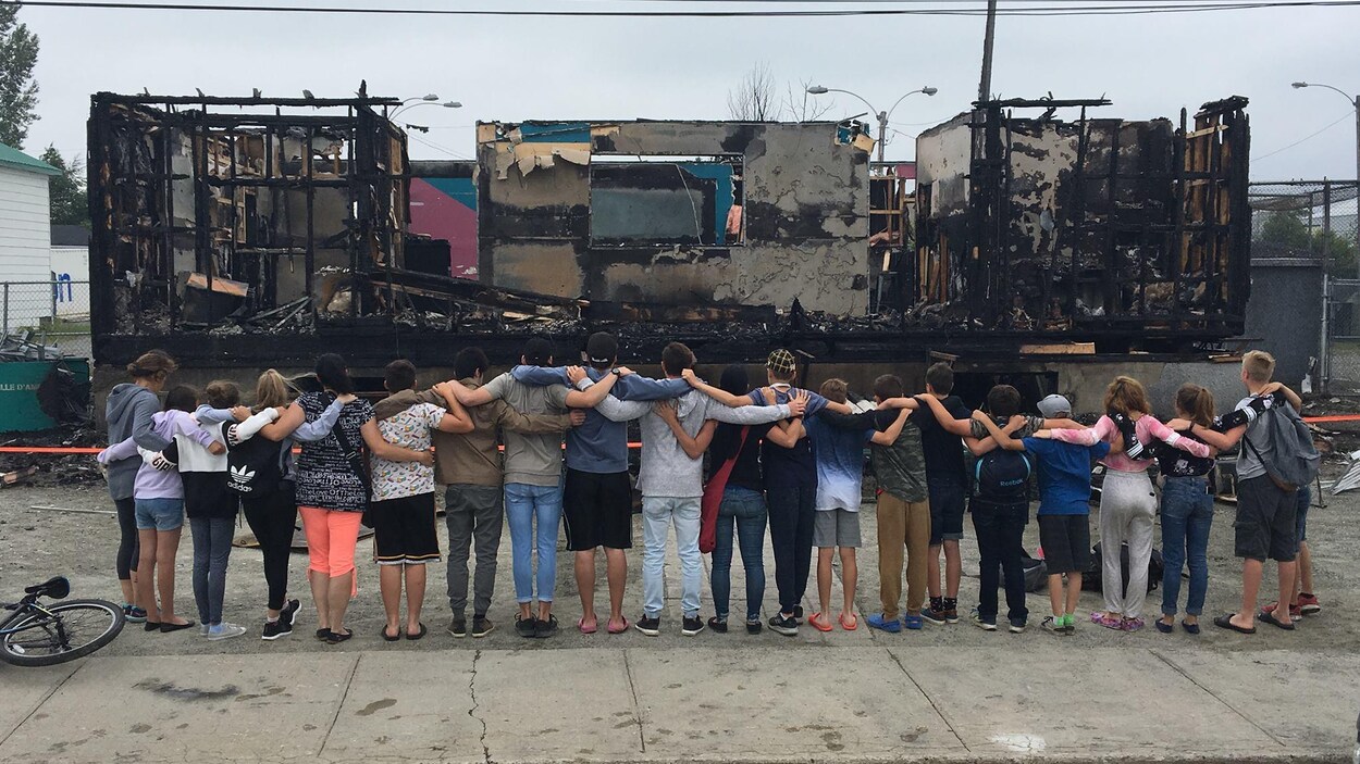 Des jeunes s'enlacent en guise de solidarité devant les restes d'un bâtiment brûlé.