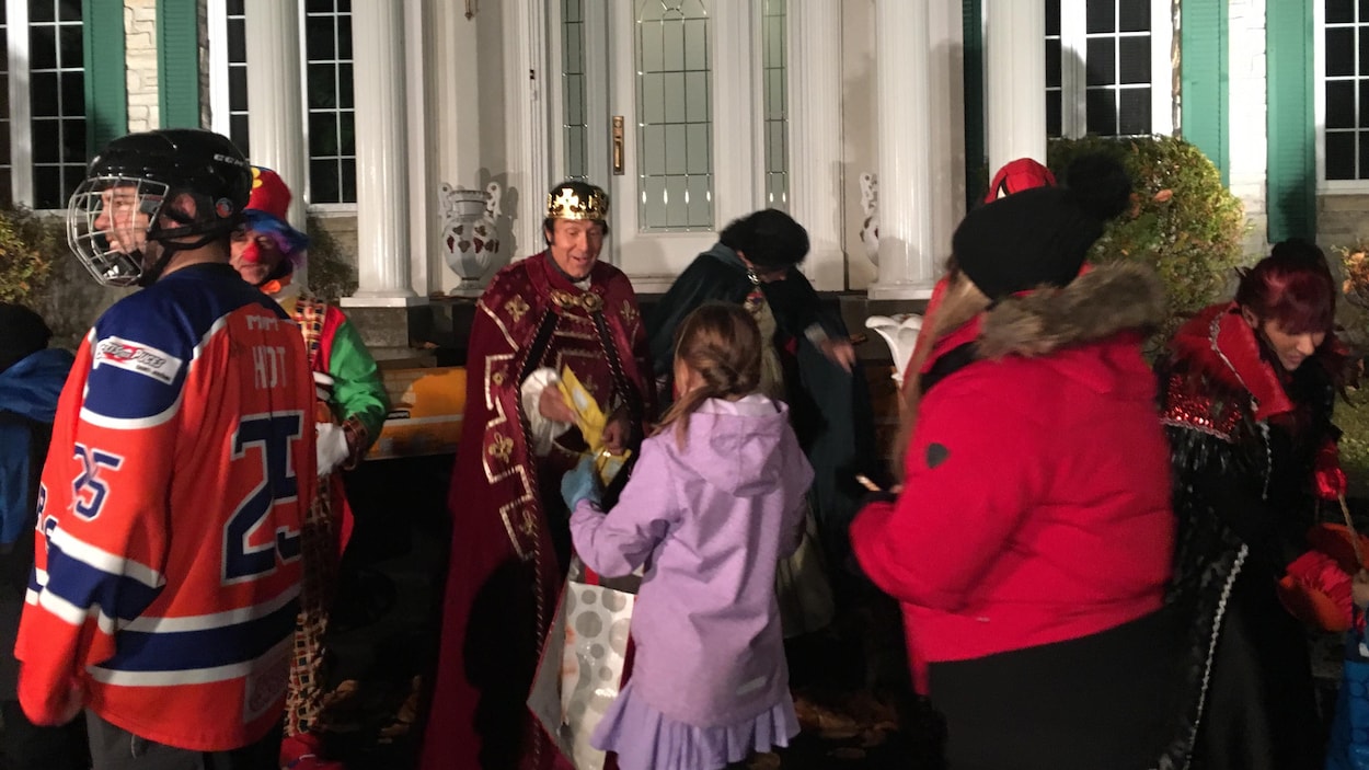 Un homme déguisé en prince distribue des friandises à une foule de personnes devant sa résidence illuminée.