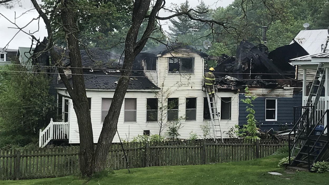 Un pompier observe une résidence brûlée à partir d'une échelle.