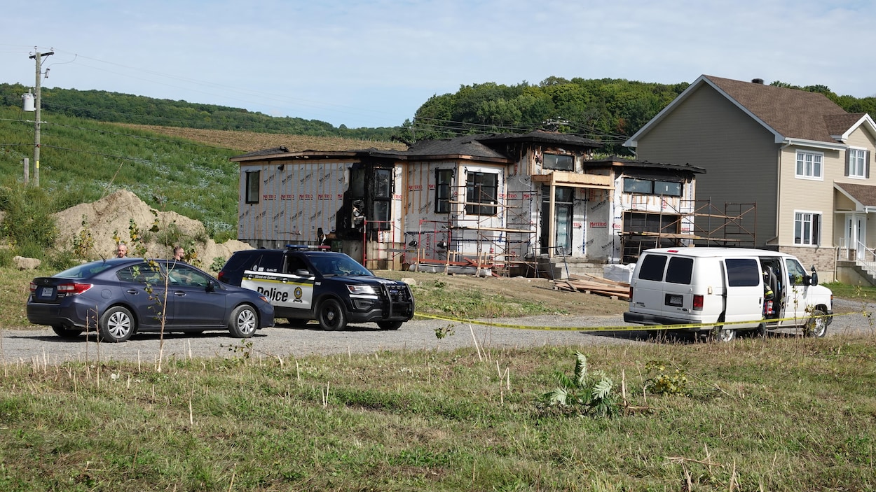 Une voiture de police et un ruban jaune devant la maison en construction partiellement brûlée.
