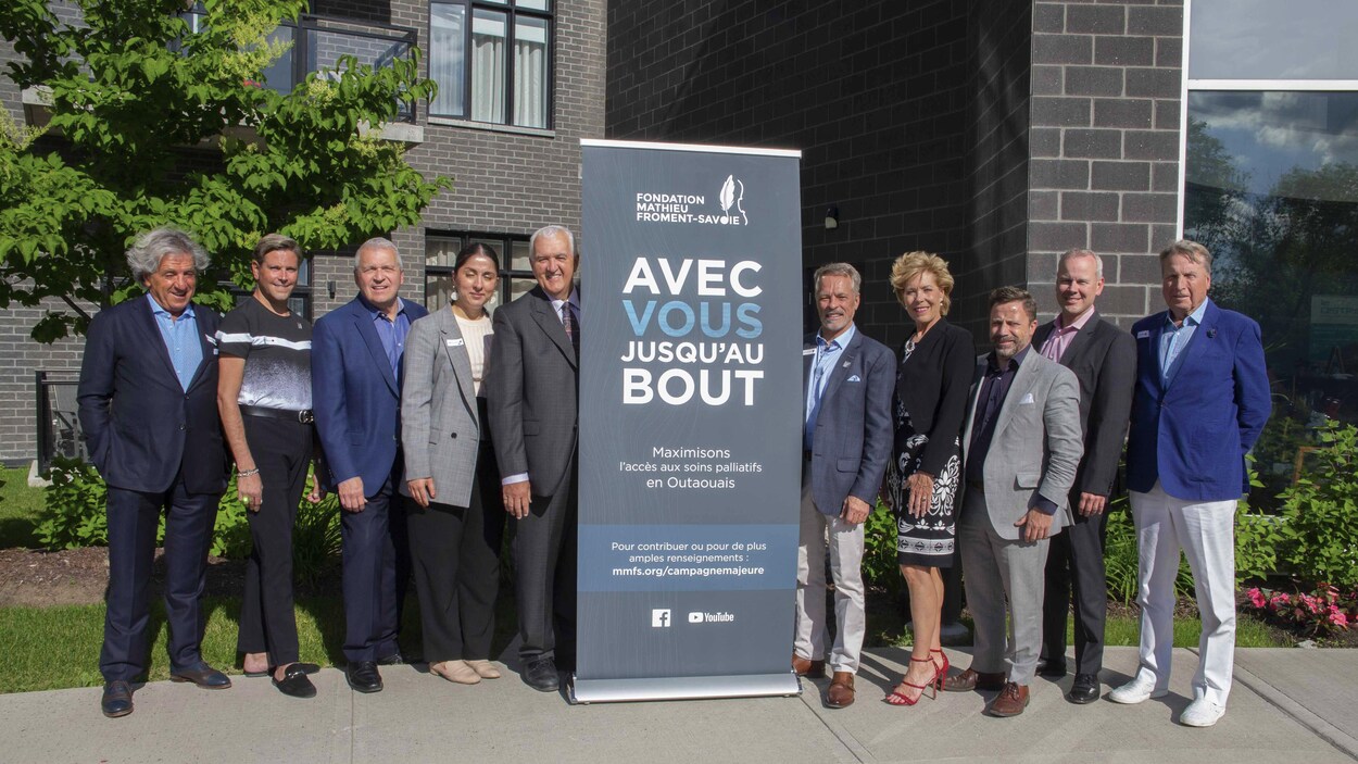 Des gens se tiennent aux côtés d'une pancarte qui annonce la campagne « Avec vous, jusqu'au bout ».