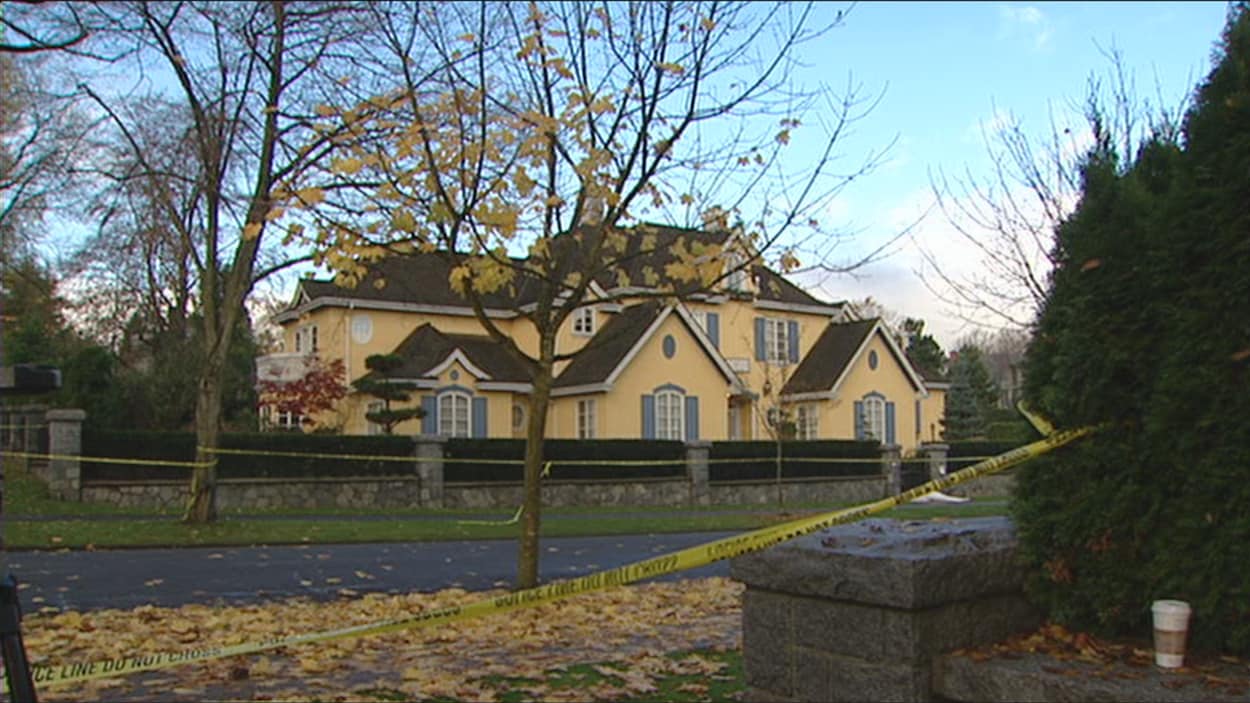 Un ruban jaune de la police interdit l'accès à un terrain entouré d'arbres au centre duquel il y a une imposante maison. Un ruban jaune de la police interdit l'accès à un terrain entouré d'arbres au centre duquel il y a une imposante maison.