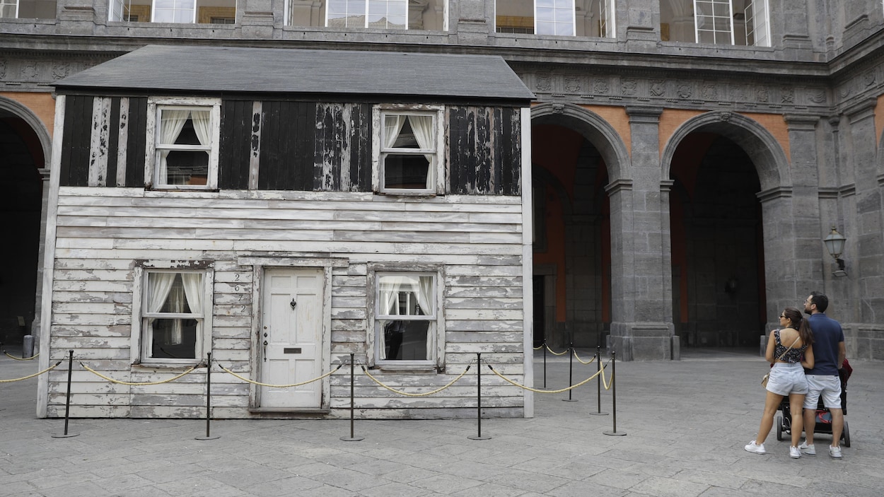 Une petite maison blanche et noire en bois, à deux étages, et éa la peinture défraîchie se tient au centre d'une place, entourée du palais royal de Naples.