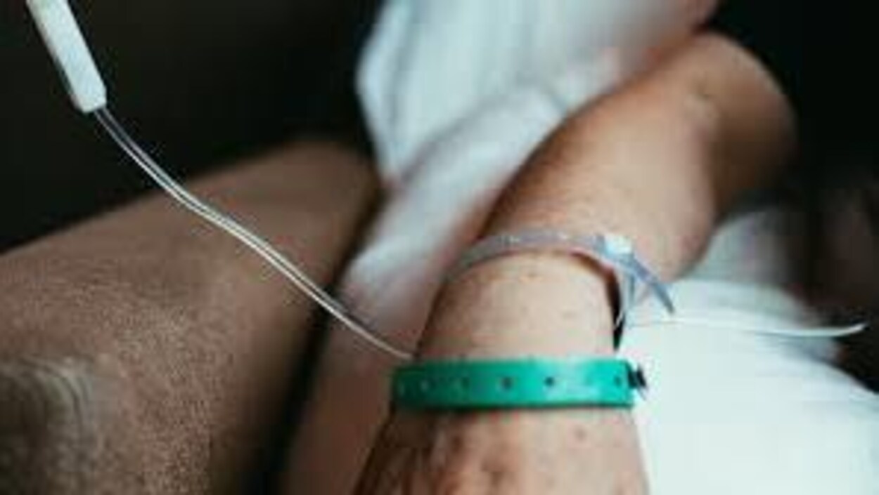 Une personne malade sur un lit d'hôpital. On ne voit que son poignet et son tube de soluté.