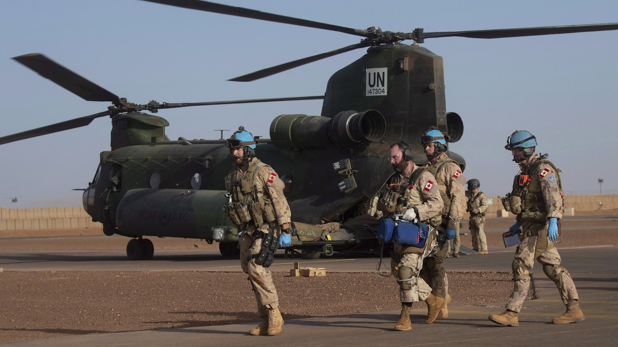 Des militaires canadiens marchent sur une base militaire devant un hélicoptère affrété par l'ONU.