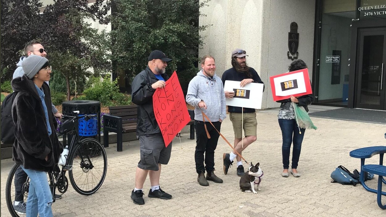 Six personnes tiennent des pancartes Free Hong Kong Democracy devant l'hôtel de ville de Regina.