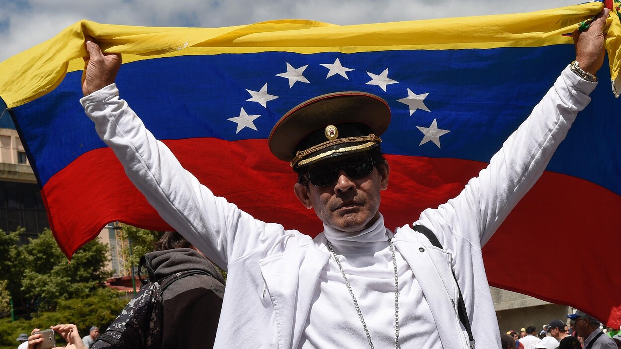Un manifestant coiffé d'une casquette militaire brandit un drapeau dans les rues de Caracas pour protester contre le gouvernement Maduro.