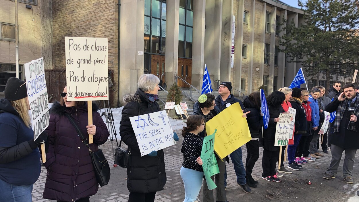 Des personnes portent des pancartes sur lesquelles on peut lire : « Mon Québec favorise la diversité », « Pas de clause de grand-père! Pas de citoyens de deuxième classe! », « The secret is in the mix » (avec dessins d'une croix, d'une étoile de David, ainsi que d'un croissant et d'une étoile), « Égalité et diversité ».