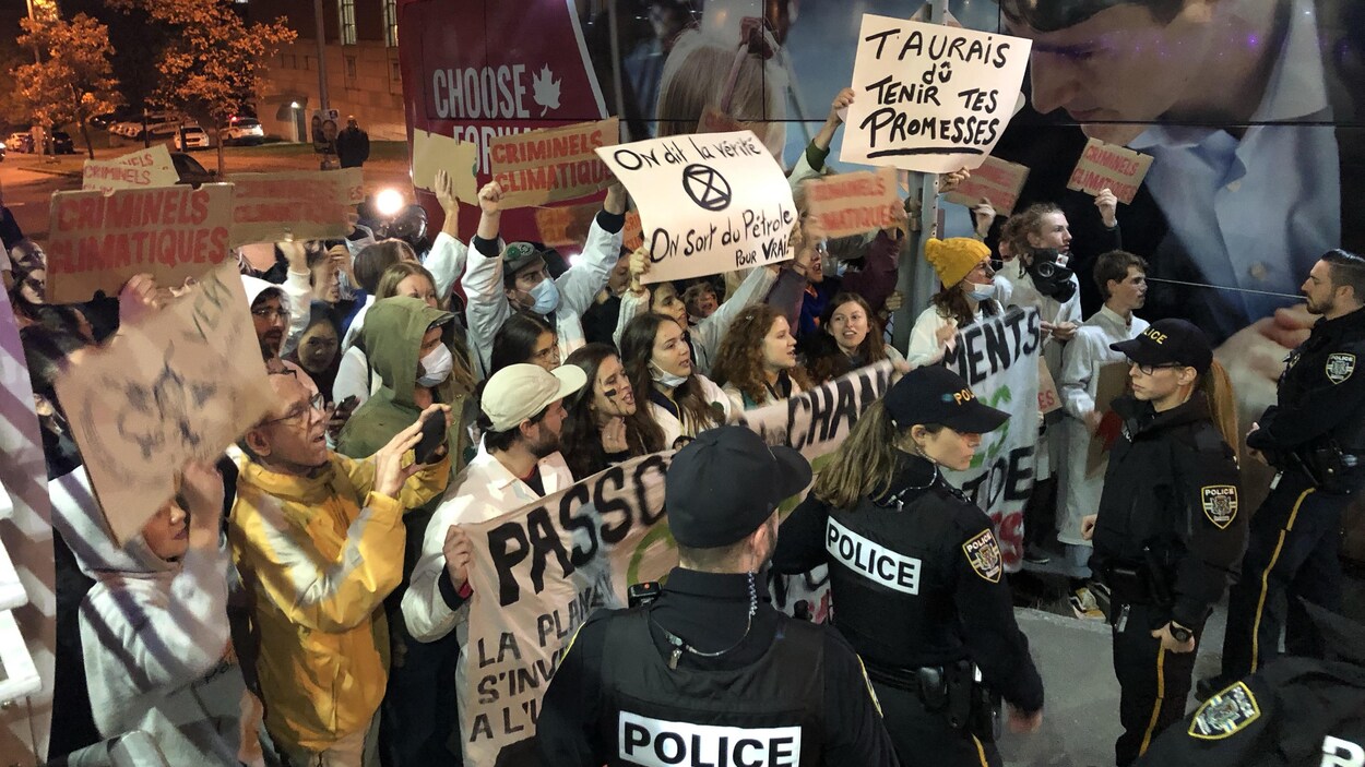 Des manifestants pour le climat arborant différentes affiches à proximité de l'autobus de campagne de Justin Trudeau.