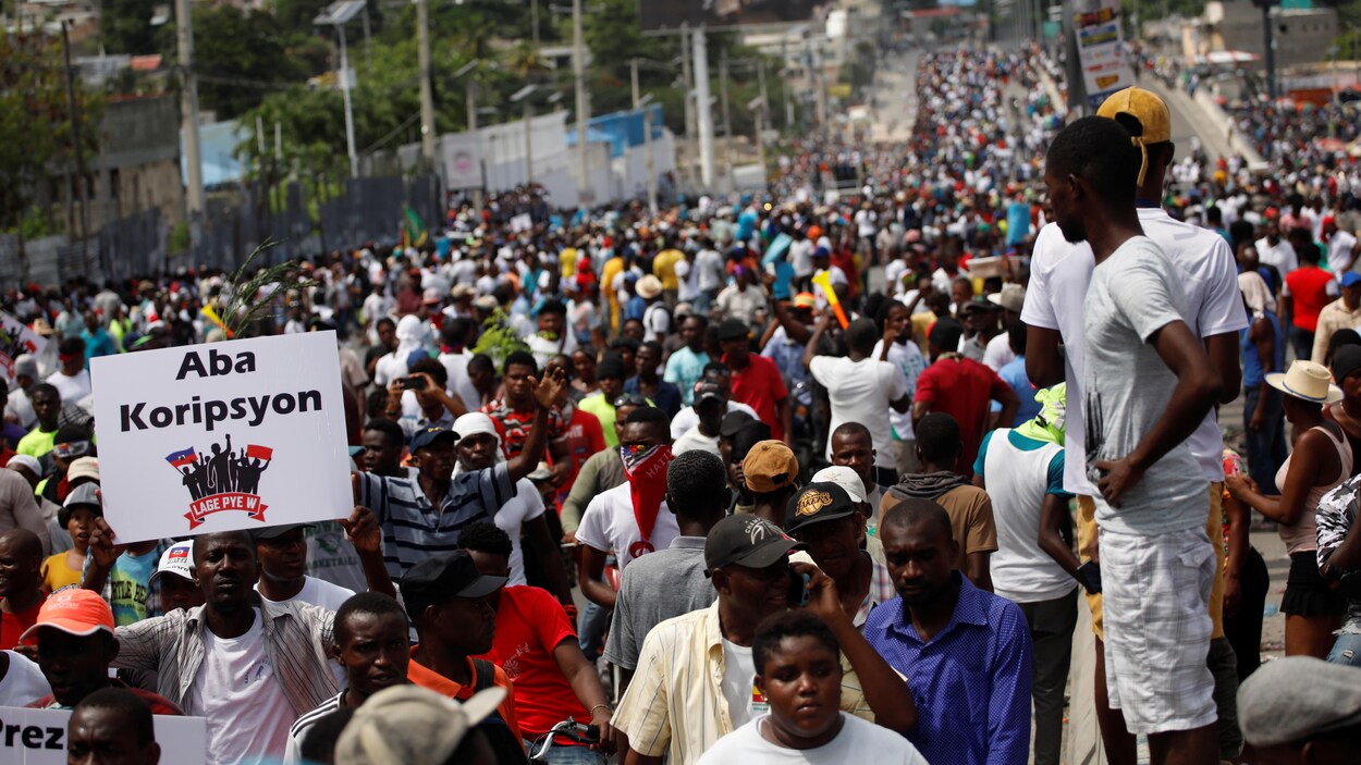 Des milliers de manifestants marchent dans une rue, certains tiennent des pancartes.