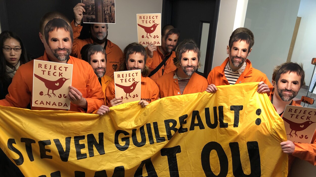 Des manifestants portant un masque représentant le visage de Steven Guilbeault et une bannière lui demandant de choisir entre le climat et Teck Resources.