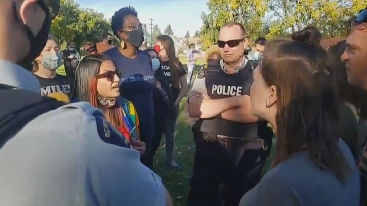 Plusieurs hommes et femmes se lancent des insultes devant deux policiers impassibles.