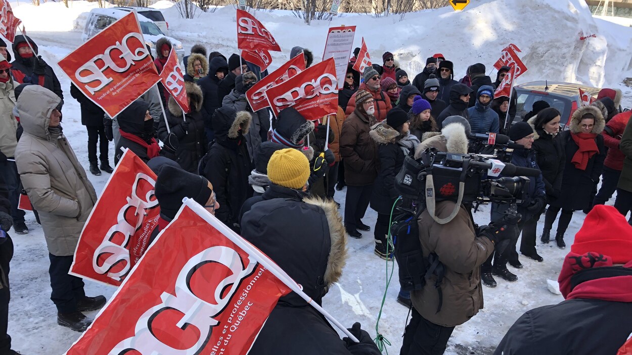 Des manifestants sont rassemblés devant l'édifice Honoré-Mercier, à Québec. Certains brandissent un fanion aux couleurs du SPGQ.