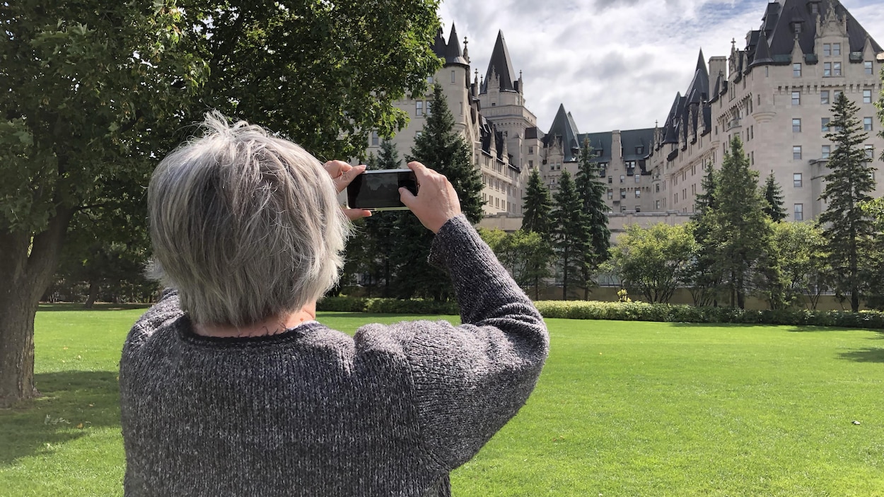 Un femme de dos à la caméra prend une photo du Château Laurier avec son téléphone intelligent.