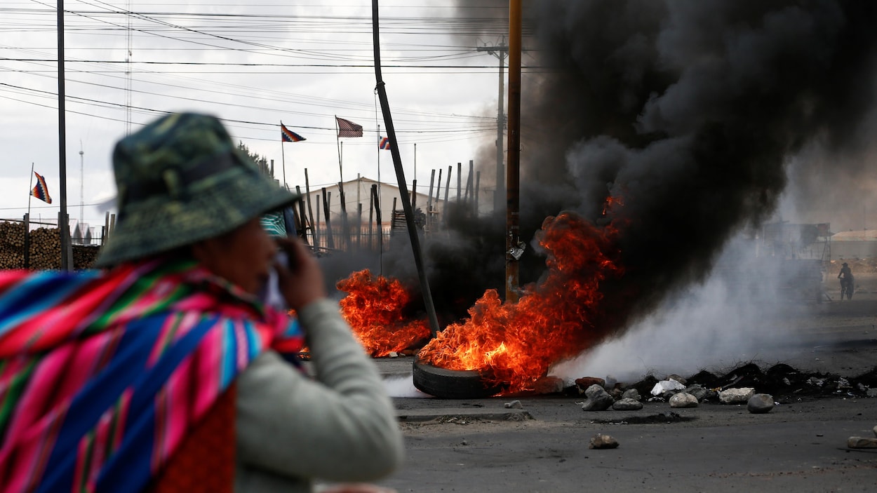 Une femme se tient dans la rue près d'une barricade de pneus en flammes.