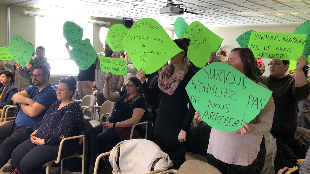Des travailleuses et des bénévoles tiennent des pancartes en forme de feuilles vertes sur lesquelles on peut lire : « Surtout, n'oubliez pas de nous arroser ».