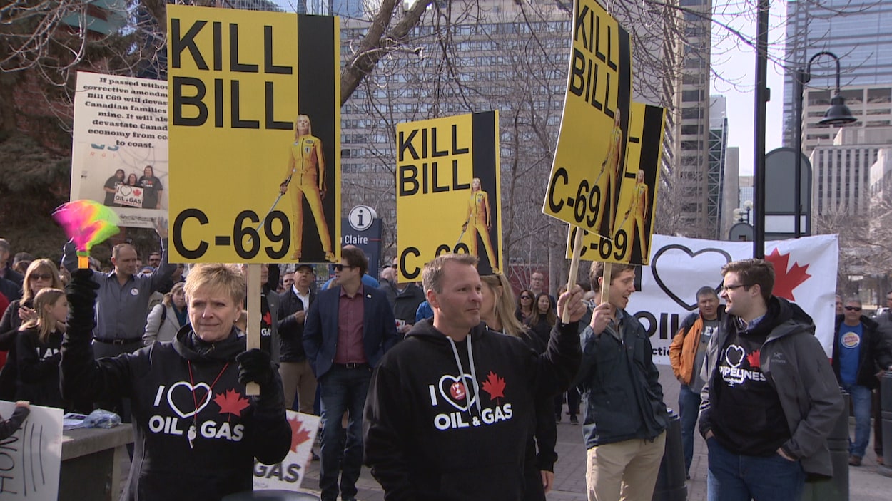 Des gens manifestent avec des pancarte jaune demandant la mort du projet de loi C-69