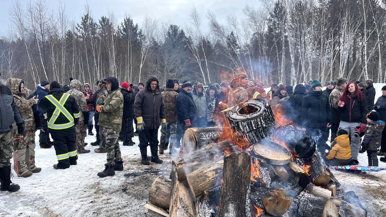 Des dizaines de manifestants chaudement habillés pour l'hiver sont autour d'un feu de bois en plein air, dans un champ.
