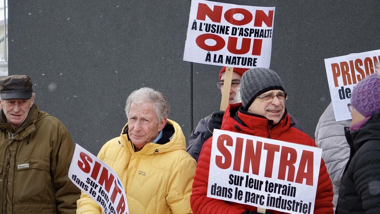 Des manifestants tiennent des pancartes, regroupés devant une tour à bureaux.