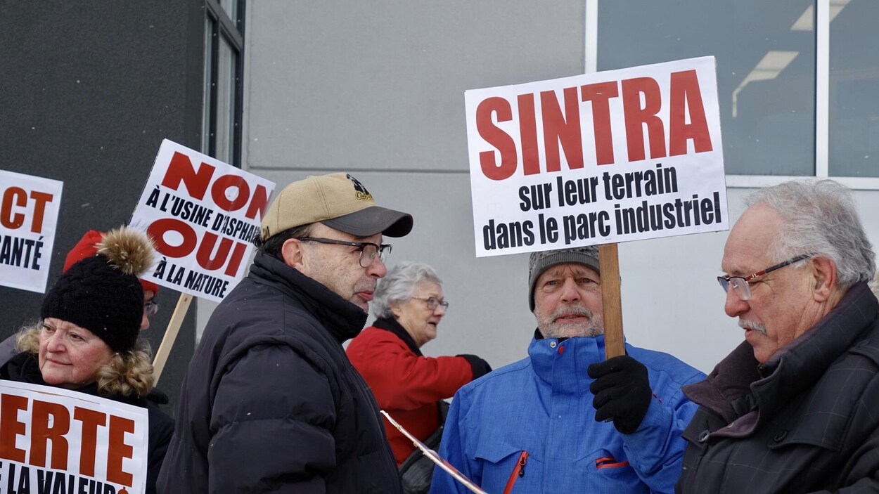 Un groupe de manifestants armés de pancartes sont regroupés devant une tour à bureaux.