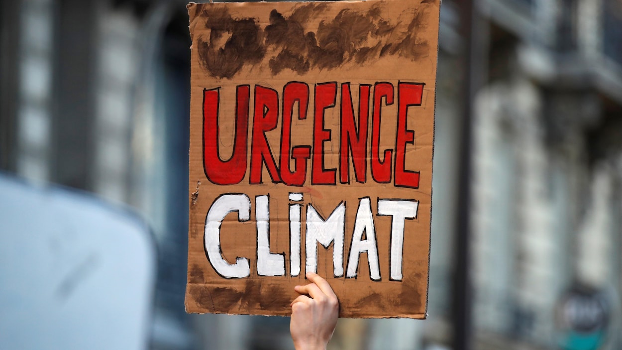 Une personne tient une pancarte sur laquelle on peut lire : « Urgence climat ».